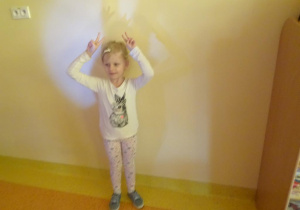 Dziewczynka stoi pod ścianą z rąk tworzy cień na ścianie.
